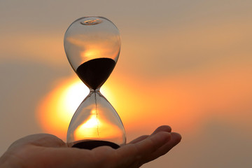Falling sand in a hourglass at sunset sky background.