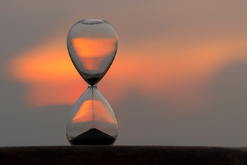 Falling sand in a hourglass at sunset sky background.