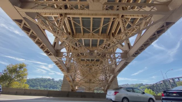 A wide shot view of traffic traveling under the Liberty Bridge in downtown Pittsburgh, Pennsylvania on a sunny day. Shot at 60fps for optional slow motion use.  	