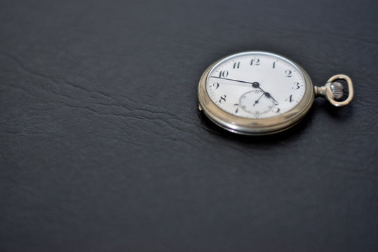 Silver pocket watch on a black surface.