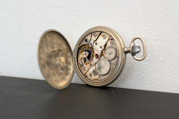 Open pocket watch, you see the machine. It is on a black surface and resting on the wall.