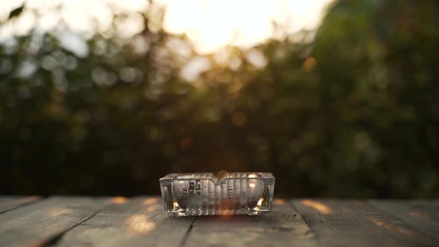 Glass cigarette ashtray on wooden table with sunset light