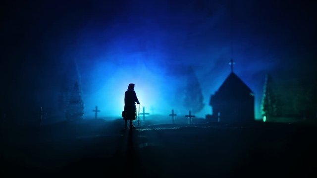 Silhouette of old woman with a cane walking at cemetery at night. Horror Halloween concept. Artwork decoration with light and fog. Selective focus