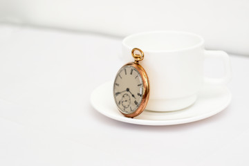 Gold pocket watch on a cup of coffee, all on a white surface.