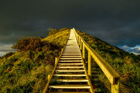 Steep golden staircase going up a hill with dark clouds in the background