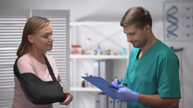 Female in arm sling telling doctor with medical form about good rehab results