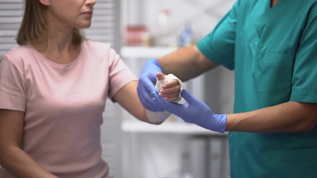 Doctor fixing elastic wrap on female patient arm, rehabilitation after trauma