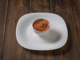Red and white sauce in a white bowl on a white plate. Vegetarian sauce.