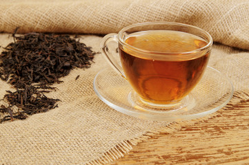 Cup of tea and dry tea leaves on rustic burlap background