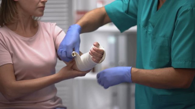Surgeon applying elastic wrap on female patient arm, rehabilitation after trauma