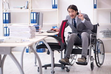 Young handsome employee in wheelchair working in the office