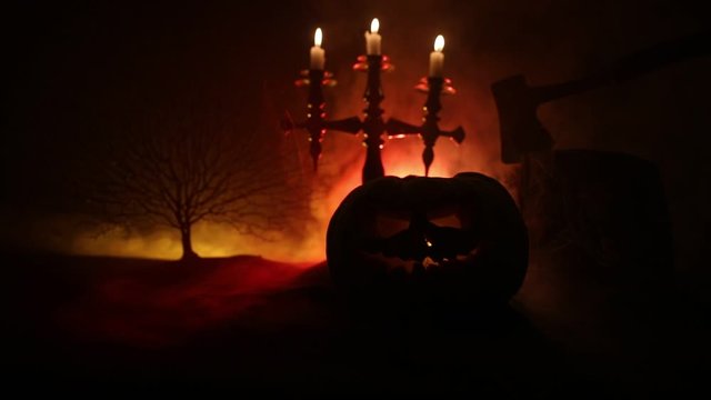 Horror concept. Scary Halloween pumpkin with carved eyes and a smile with burning candles and an ax on a dark toned background. Empty space. Selective focus