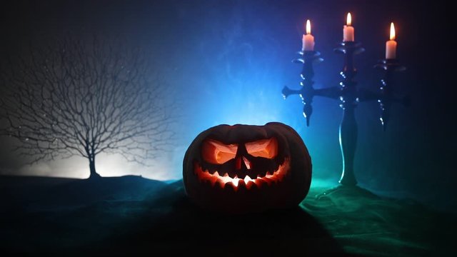 Horror concept. Scary Halloween pumpkin with carved eyes and a smile with burning candles and an ax on a dark toned background. Empty space. Selective focus