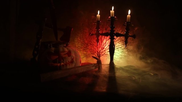 Horror concept. Scary Halloween pumpkin with carved eyes and a smile with burning candles and an ax on a dark toned background. Empty space. Selective focus