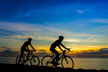 Cyclists with bicycles at the beach, at dusk.
