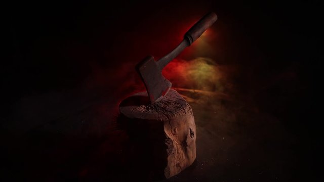 Old ax attached to the tree trunk on horror red foggy background. Scary Halloween theme with maniac killer weapon. Empty space. Selective focus