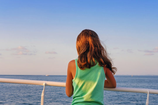 A little girl leaning on the railing while looking at the horizon