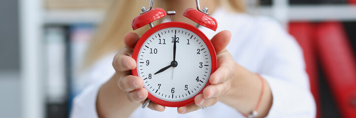 Smiling business woman holding in hand on the alarm clock a red color showing eight o'clock in the...