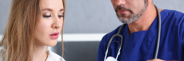 Smiling handsome doctor communicate with patient holding silver pen and showing pad. Physical...
