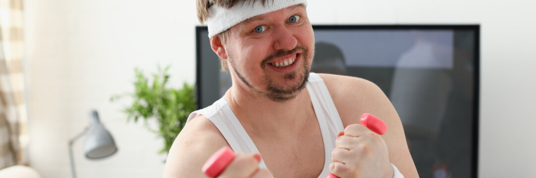 Young attractive man engaged in fitness at home holding dumbbell in hand trying to fight excess weight and loss