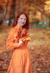 A bright girl with copper-colored hair. Beautiful autumn nature.