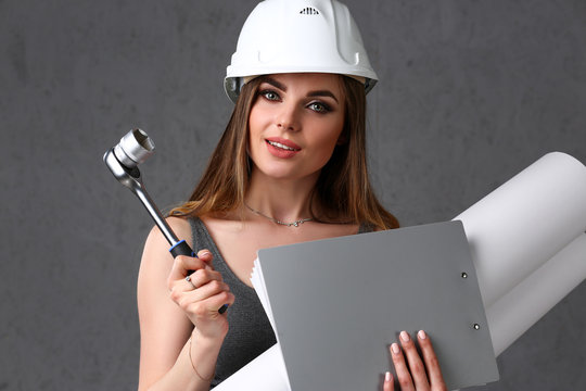 Young beautiful brunette girl wearing white helmet portrait over grey background. Manual job DIY inspiration improvement fix wrench startup instrument pad industrial profession career tool help