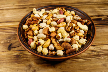 Mixed nuts on wooden table. Walnuts, pistachio, almond, peanut, cashew, hazelnut in ceramic bowl. Healthy eating concept