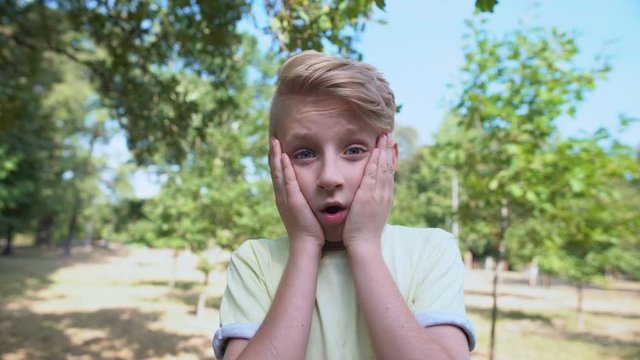 Surprised caucasian boy feeling shocked standing in park, emotions concept