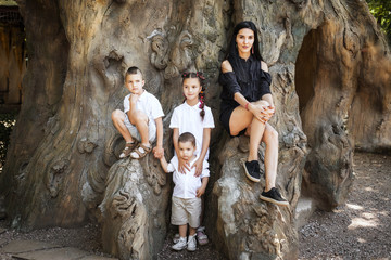 beautiful mother with her three happy joyful cute children sitting in the tree in the park. concept of love and family