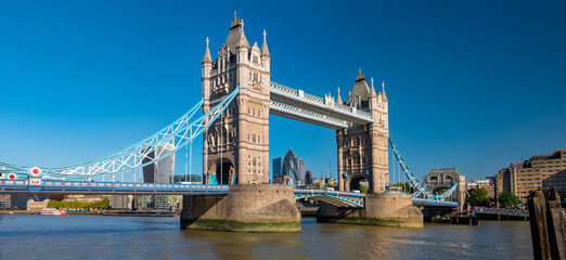 Panorama view of the Tower bridge over Thames river on a sunny day with the City Financial district skyscrapers and Tower of London in the background.