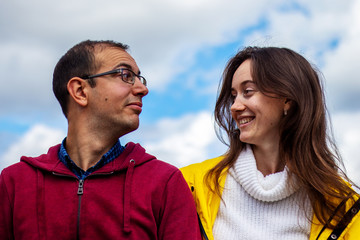 Fototapeta premium Man with glasses and beautiful girl are looking at each other, cloudy sky background. Friendship between man and woman concept.