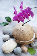 Natural coconut with coconut water, vertical shot on a beige stone background with pebbles and orchid