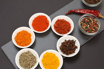 Various ground spices and herbs on stone cutting board.