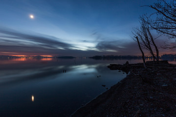Moon above a lake with its reflection on the Trasimeno lake surface at dusk