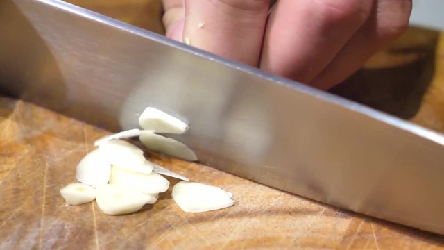 Chef Chopping Garlic with a Damascus Steel Knife on a Wooden Board - Close-Up Detail