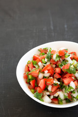 Pico de Gallo in a white bowl on a black surface, low angle view. Space for text.