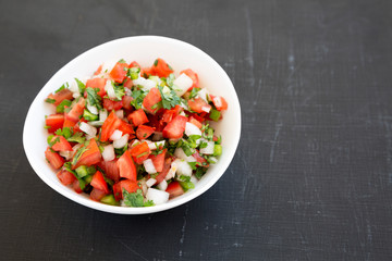 Pico de Gallo in a white bowl on a black background, low angle view. Copy space.