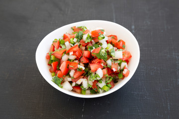Pico de Gallo in a white bowl on a black background, side view. Close-up.