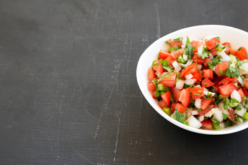 Pico de Gallo in a white bowl on a black surface, side view. Copy space.