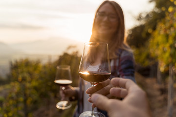 Woman passing a red wine glass at her boyfriend. vineyard during sunset