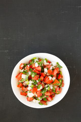 Pico de Gallo in a white bowl on a black background, top view. Overhead, from above, flat lay. Space for text.