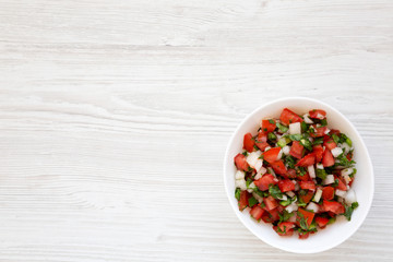 Pico de Gallo in a white bowl on a white wooden background, top view. Overhead, from above, flat lay. Copy space.