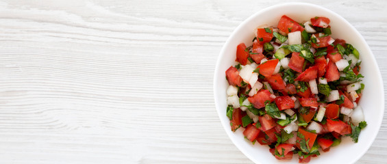 Pico de Gallo in a white bowl on a white wooden surface, top view. Overhead, from above, flat lay. Space for text.