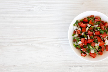Pico de Gallo in a white bowl on a white wooden surface, top view. Overhead, from above, flat lay. Space for text.