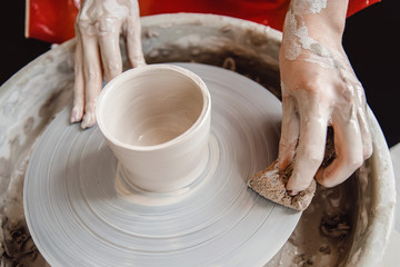 Work at potter wheel in apron. Hands of young woman with clay. Top view