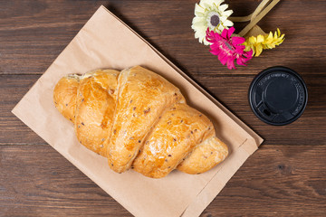 croissant in paper bag on wooden background with paper disposable cup of coffee. concept of continental breakfast and eco packaging