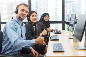 Group of multicultural call center people sitting at their desk with headset giving thumbs up for successful business and work Teamwork ready to help and support customers with best solution concept