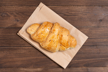 croissant in paper bag on wooden background. concept of continental breakfast and eco packaging, recycling of raw materials