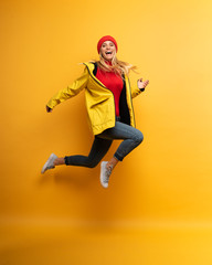 Girl with jacket jumps to the sun from the rainy weather. Joyful expression. Yellow background