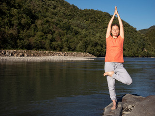 Fototapeta na wymiar Young woman is practicing yoga in pose at mountain lake